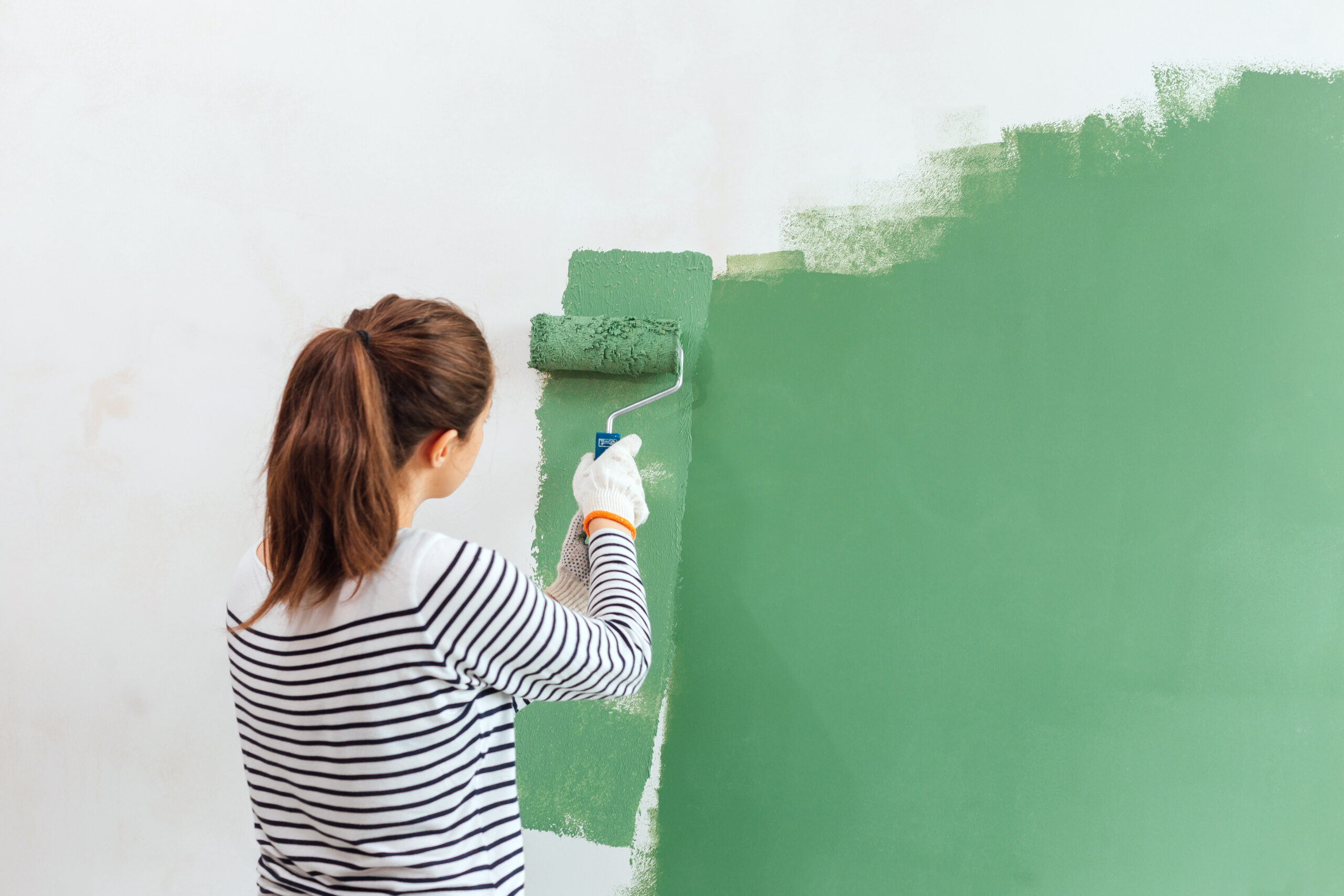 mujer-joven-que-pinta-la-pared-interior-con-el-rodillo-de-pintura
