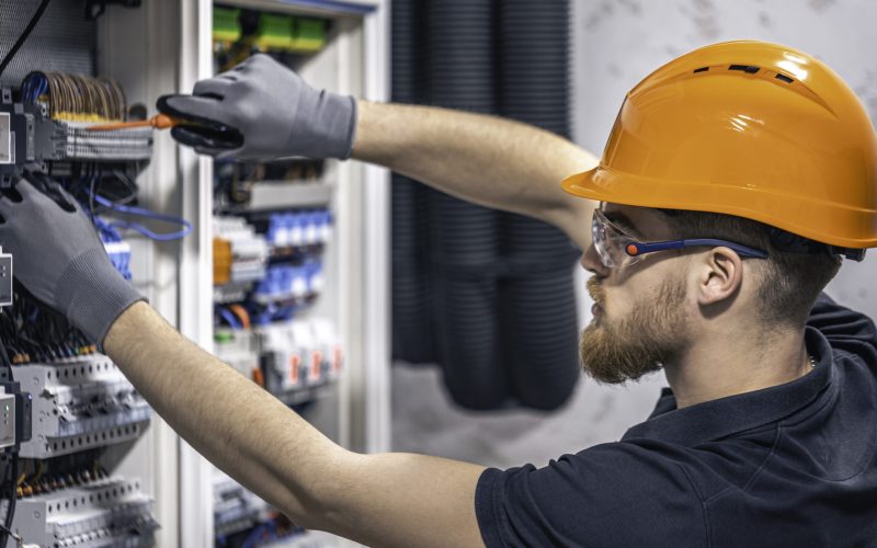 A male electrician works in a switchboard with an electrical connecting cable.