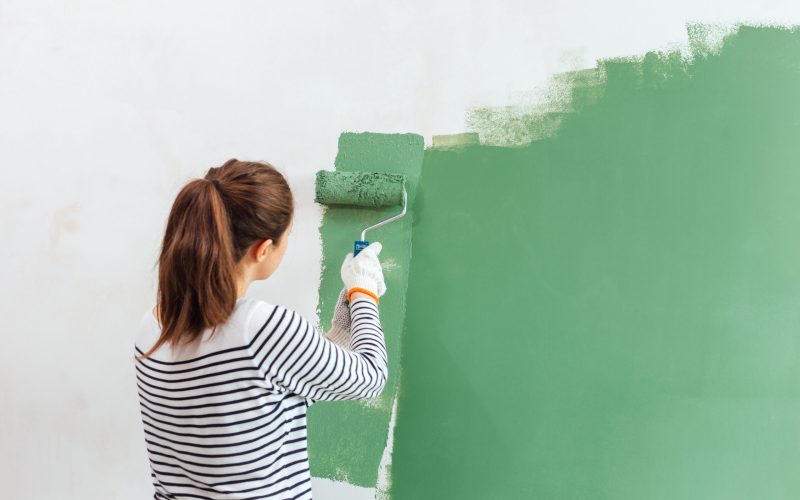 mujer-joven-que-pinta-la-pared-interior-con-el-rodillo-de-pintura